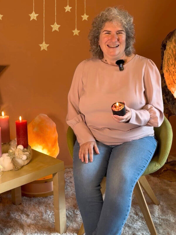 Carola Harter sitzt mit einer Kerze in der Hand in gemütlichem Kerzenambiente und channelt Engel