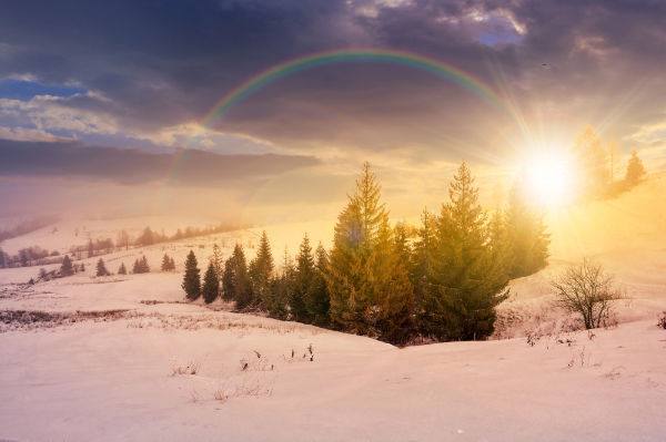 Winterlandschaft mit Sonnenaufgang und Regenbogen in verschneiter Landschaft