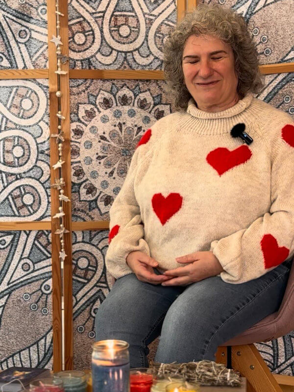 Carola Harter sitzt mit einer Kerze in der Hand in gemütlichem Kerzenambiente und channelt Engel